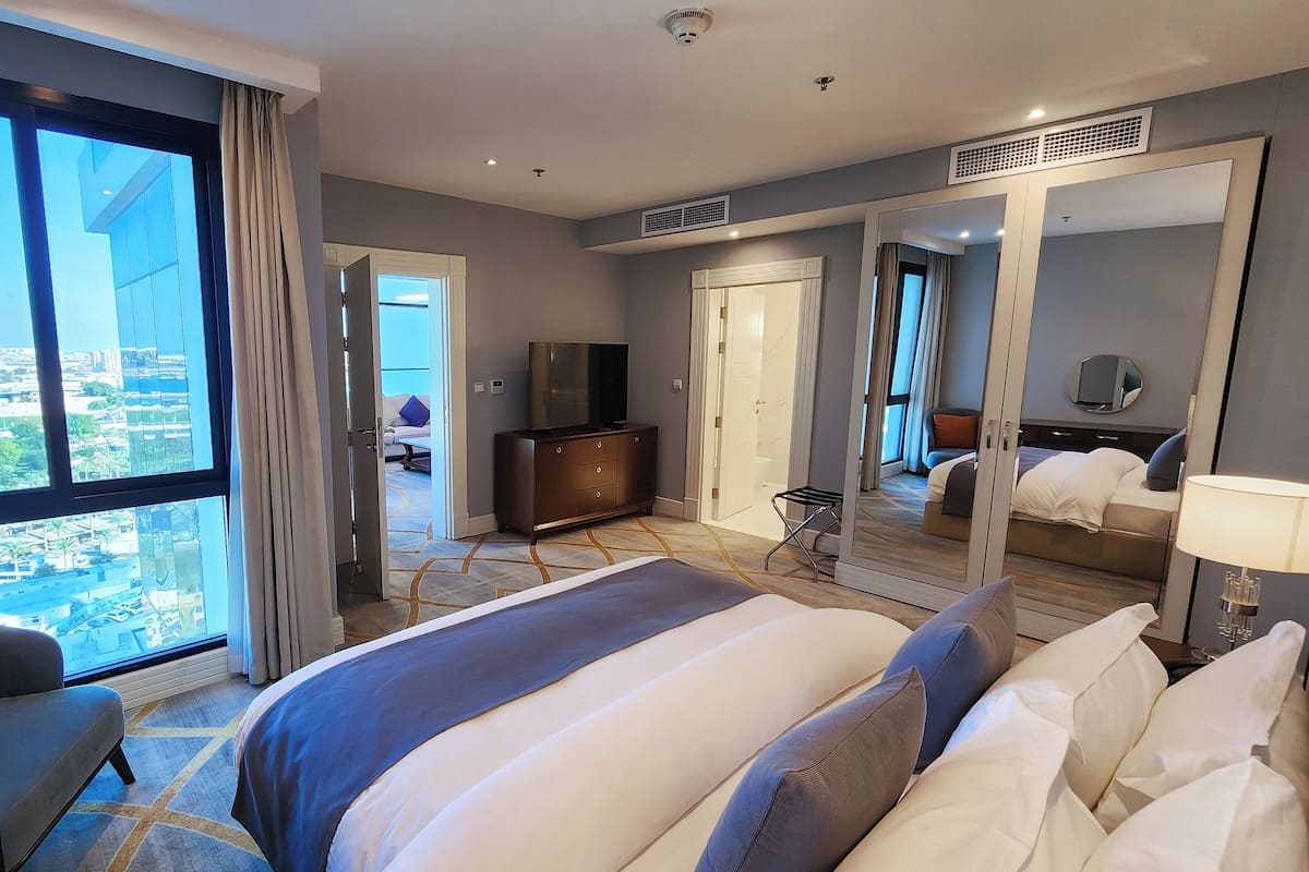 A hotel room with a large bed, a TV, a desk, and a view of the city.