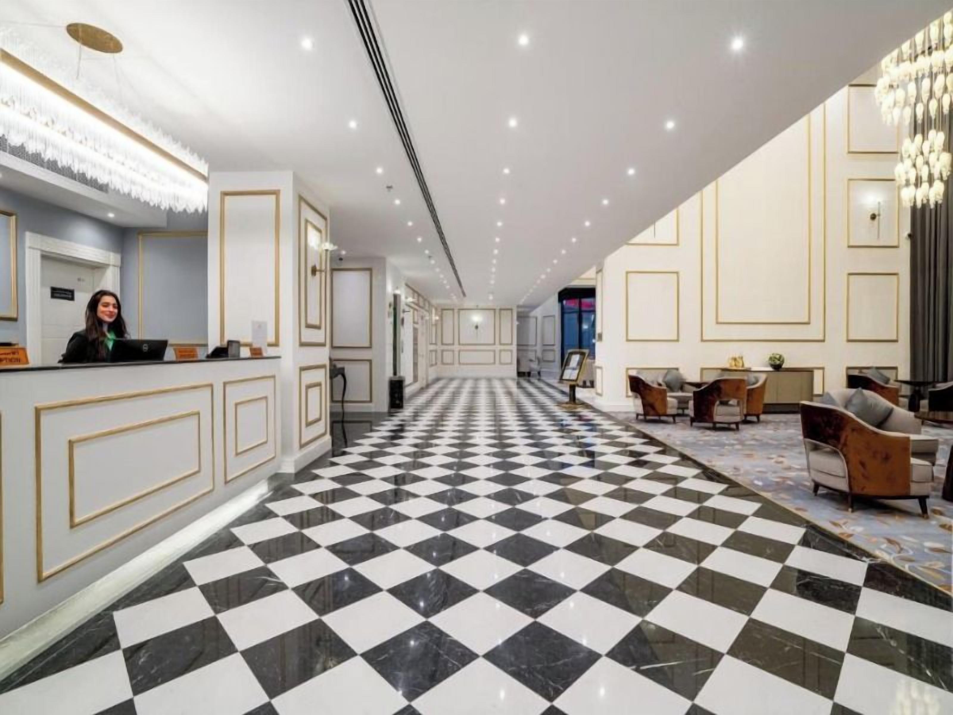 Um saguão de hotel com piso quadriculado, balcão de recepção e áreas de estar.