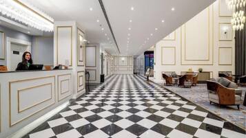 Um saguão de hotel com piso quadriculado, balcão de recepção e áreas de estar.