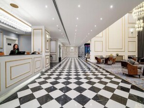 Um saguão de hotel com piso quadriculado, balcão de recepção e áreas de estar.