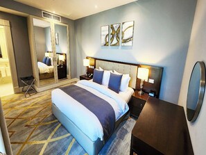 A hotel room with a large bed, bedside tables with lamps, a mirror, and abstract wall art. - Shraao Hotel (Doha)