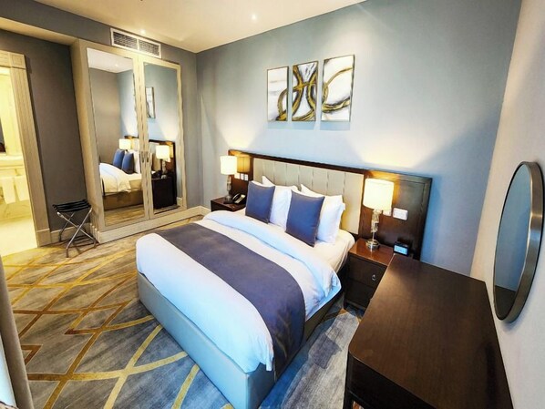 A hotel room with a large bed, bedside tables with lamps, a mirror, and abstract wall art. - Shraao Hotel (Doha)
