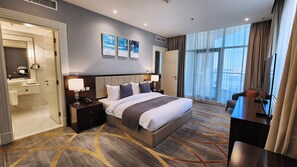A hotel room with a large bed, bedside tables, a desk, a chair, a bathroom with a mirror, and artwork on the wall. - Shraao Hotel (Doha)