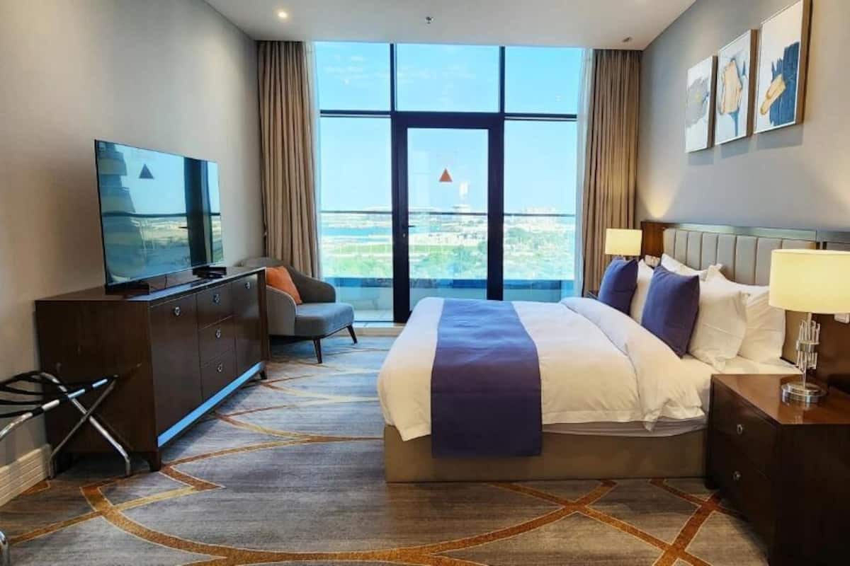 A hotel room with a large bed, a TV, a desk, and a view of the city.