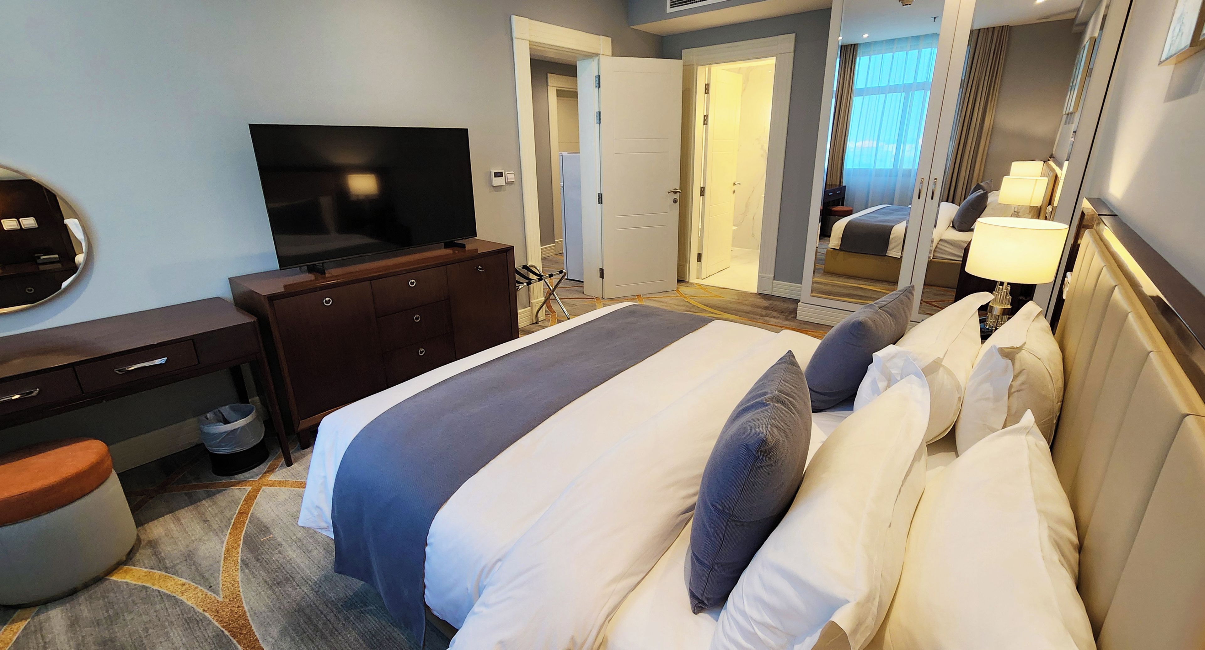 Quarto de hotel com cama, televisão, penteadeira e espelho.