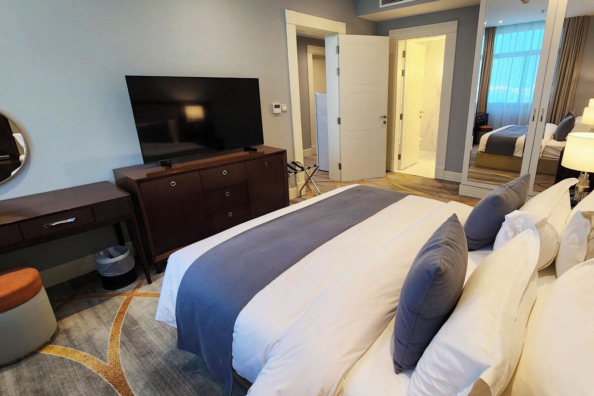 A hotel room with a bed, a TV, a dresser, and a mirror.