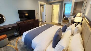 Quarto de hotel com cama, televisão, penteadeira e espelho.