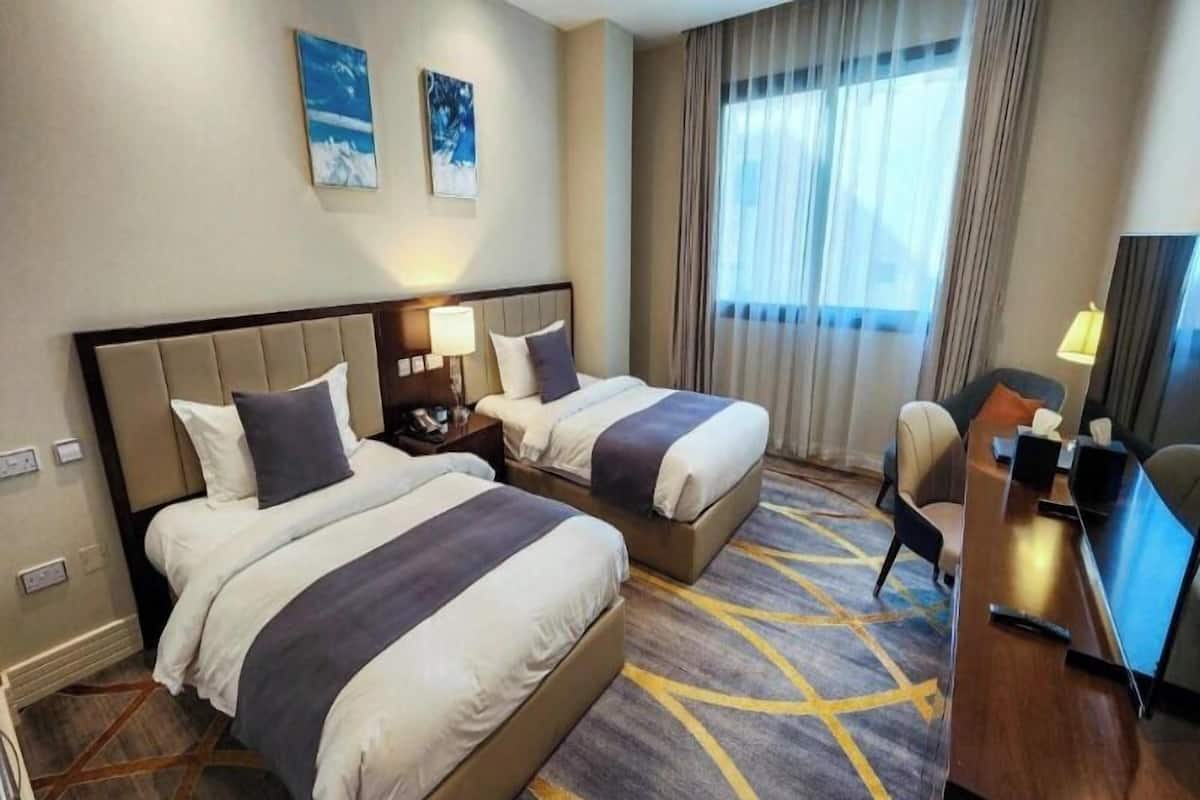 A hotel room with two beds, a desk, a chair, and a TV.