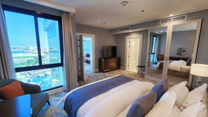 A hotel room with a large bed, a TV, a desk, and a view of the city. - Shraao Hotel (Doha)