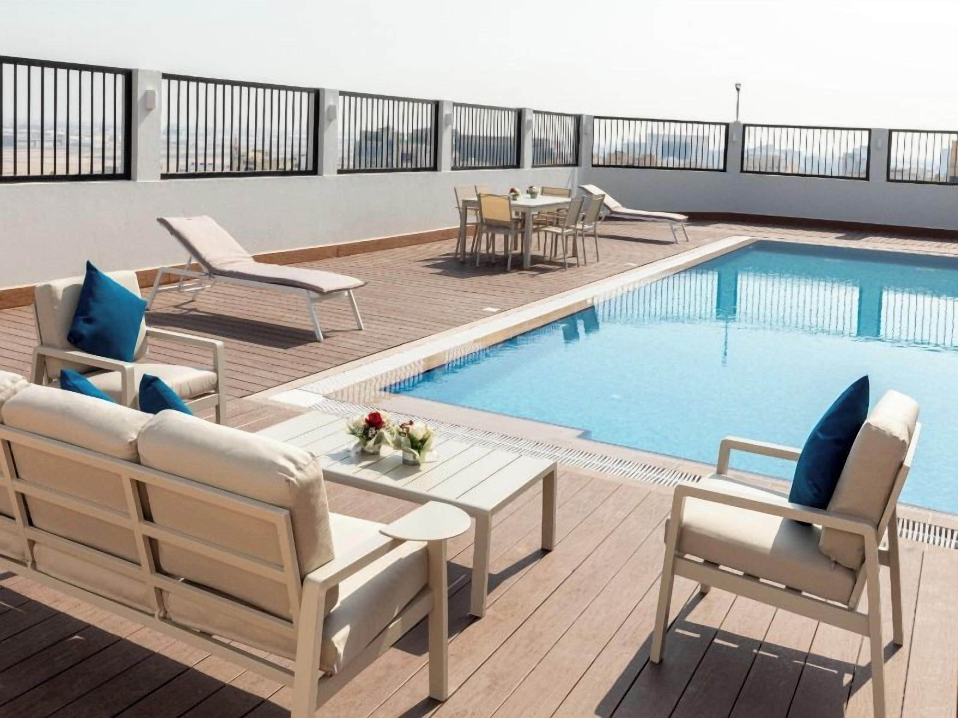 Uma área de piscina no terraço com espreguiçadeiras, uma mesa e um pequeno conjunto de jantar.
