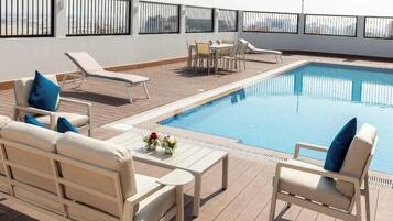 Uma área de piscina no terraço com espreguiçadeiras, uma mesa e um pequeno conjunto de jantar.