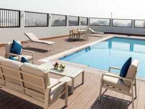 Uma área de piscina no terraço com espreguiçadeiras, uma mesa e um pequeno conjunto de jantar.
