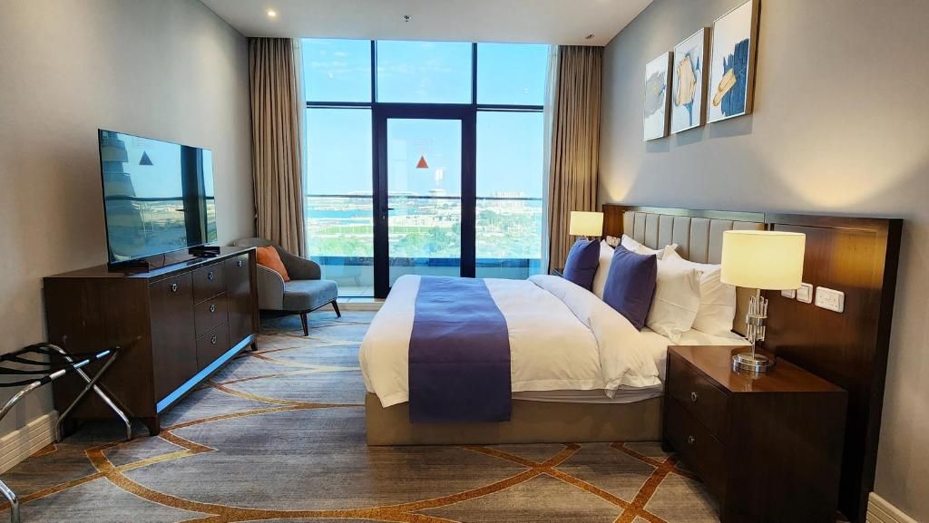 Habitación de hotel con una cama grande, televisor, escritorio y vistas de la ciudad.