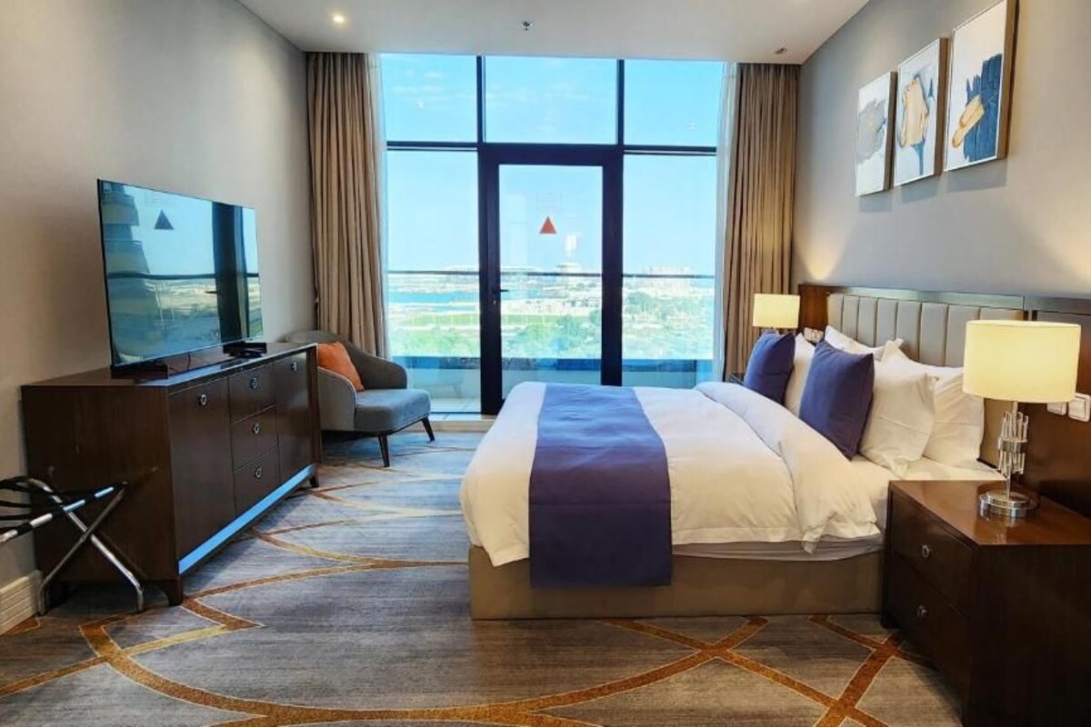 A hotel room with a large bed, a TV, a desk, and a view of the city.