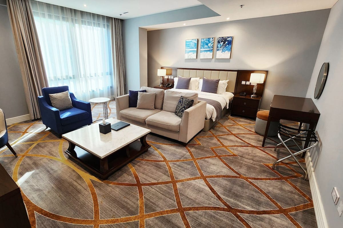 A hotel room with a bed, a sofa, a chair, a coffee table, and a desk.