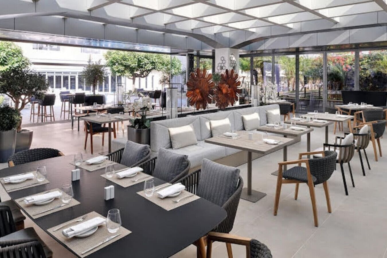 Een buiten eethoek met tafels en stoelen, een zithoek met banken, en potplanten.