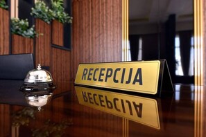 A reception desk with a sign that reads "RECEPCIJA" and its reflection on a polished surface. - Lazaro Hotel Podgorica (Podgorica)