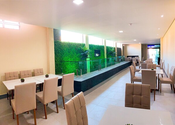 A spacious indoor dining area with long tables and chairs, a green vertical garden wall, and a glass railing overlooking a lower level. - Atlantico Sul Hotel Porto de Galinhas (Ipojuca)