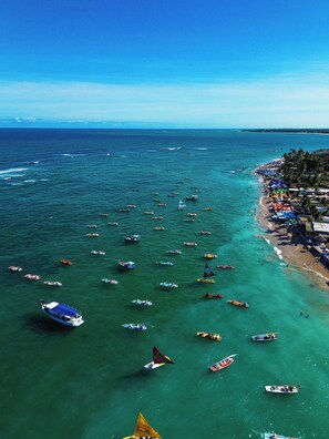 A coastal area with numerous boats on the water and a beach with umbrellas and people. - Atlantico Sul Hotel Porto de Galinhas (Ipojuca)