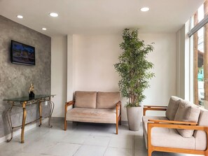 Ein modernes Wohnzimmer mit einem beigen Sofa, einem Holztisch und einer großen Kübelpflanze.