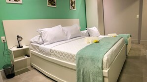 A neatly made bed with white bedding and a green throw blanket, a bedside table with a lamp, and a trash bin. - Atlantico Sul Hotel Porto de Galinhas (Ipojuca)