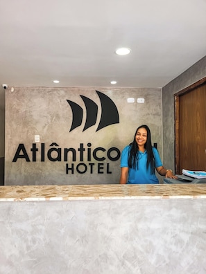 A reception desk at Atlantico Hotel with a modern design, a large logo, and a wooden door in the background. - Atlantico Sul Hotel Porto de Galinhas (Ipojuca)