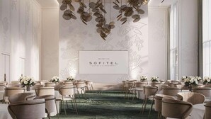 Un espacio para eventos formales con alfombra verde, arreglos florales blancos y un letrero que dice "SOFITEL HOTELS & RESORTS".