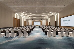 Una sala conferenze con file di sedie, un grande schermo di fronte e un pavimento con moquette.