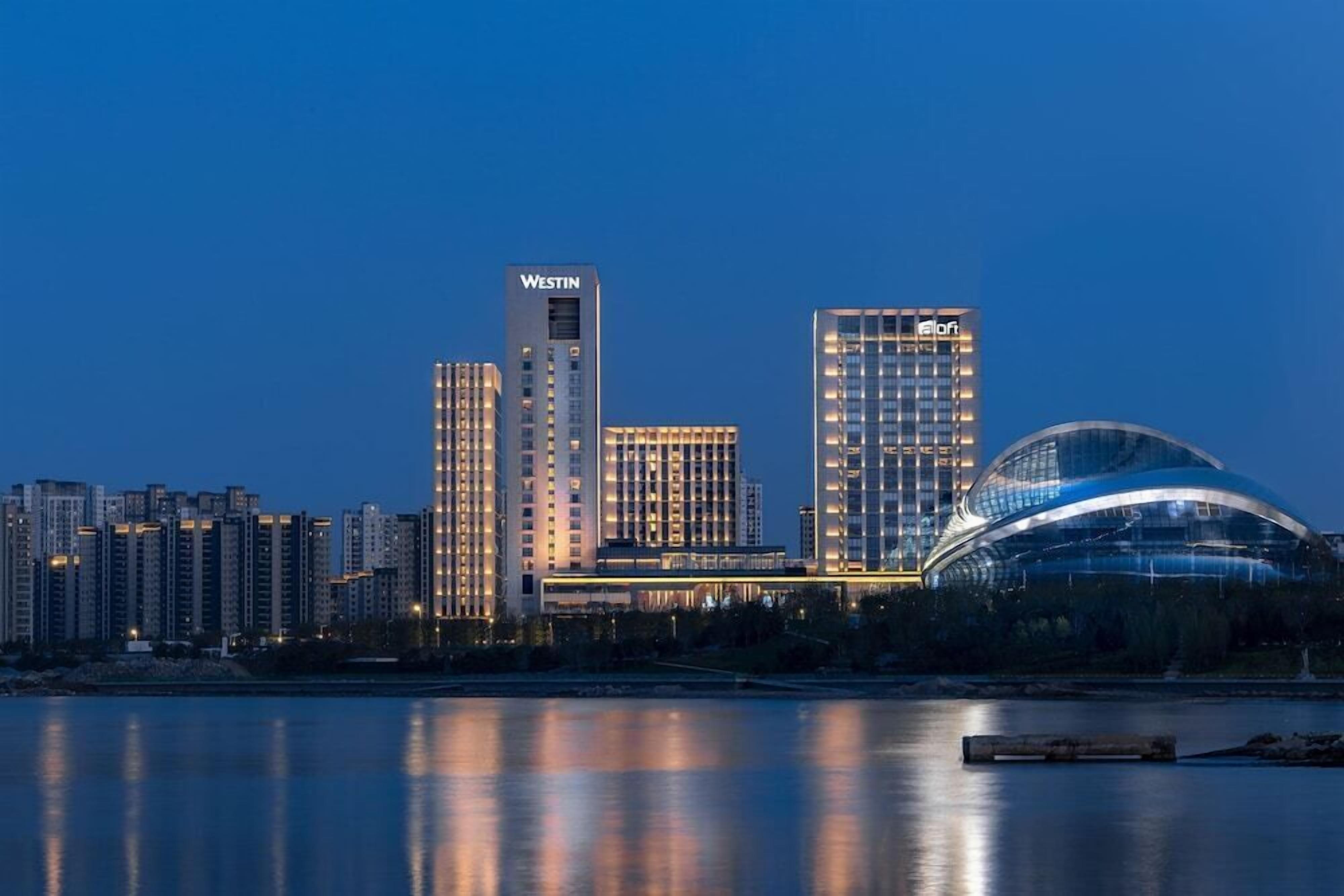 A modern hotel with a prominent Westin sign, a large glass dome structure, and a waterfront view.