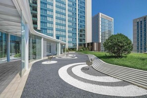 Un edificio moderno con facciata in vetro curvo, un'area verde con un percorso sinuoso e un albero.