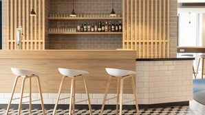 A bar area with a wooden counter, three white stools, and shelves with bottles and glasses. - Holiday Inn Express & Suites Deventer (Deventer)