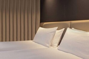 Habitación de hotel con una cama grande, cabecera oscura y persianas verticales.