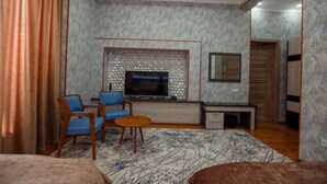 A modern living room with a TV, blue chairs, a coffee table, and a patterned rug. - ADA Hotel Tashkent (Tashkent)