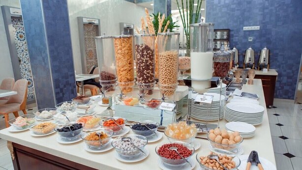 A buffet with various food items and containers, including bowls and jars, in a room with blue walls and a tiled floor. - ADA Hotel Tashkent (Tashkent)
