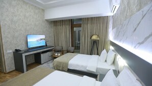 A hotel room with two beds, a desk with a TV, a lamp, and a view of the sea through the window. - ADA Hotel Tashkent (Tashkent)