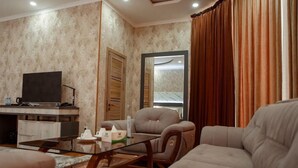 A living room with a sofa, armchair, coffee table, television, and a mirror. - ADA Hotel Tashkent (Tashkent)