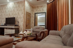 Ein Wohnzimmer mit Sofa, Sessel, Couchtisch, Fernseher und einem Spiegel.