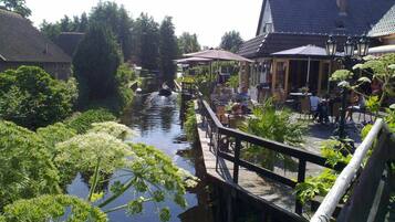 A riverside walkway with outdoor seating, a bridge, and buildings with traditional architecture.