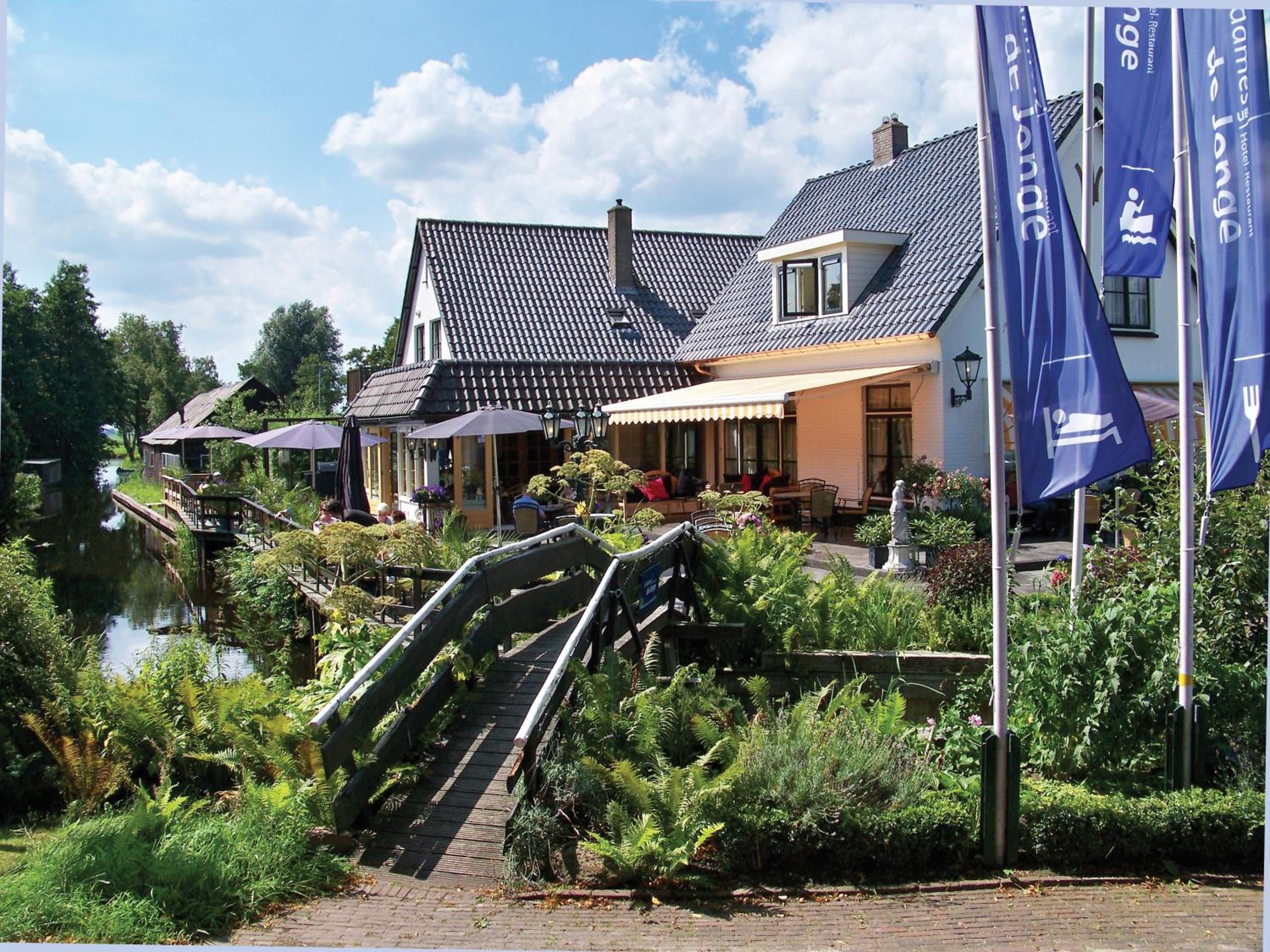 A riverside hotel with outdoor seating, a bridge, and flags.