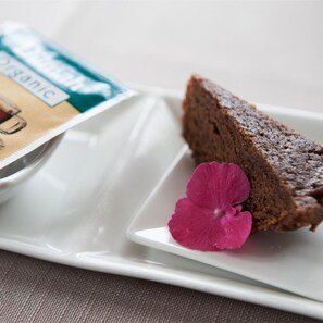 A slice of dark chocolate cake on a white plate with a pink flower, and a magazine with 'organic' visible. - De Dames Van De Jonge Hotel Restaurant (Giethoorn)