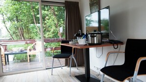 A room with a wooden table, two chairs, a TV, and a window with a view of greenery. - De Dames Van De Jonge Hotel Restaurant (Giethoorn)