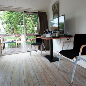 A room with a wooden table, two chairs, a TV, and a window with a view of greenery. - De Dames Van De Jonge Hotel Restaurant (Giethoorn)