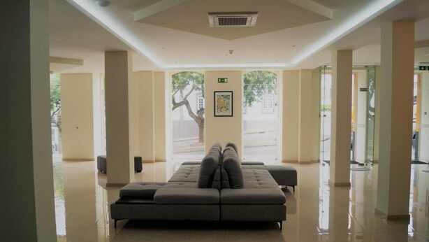 A spacious lobby with a large sectional sofa, a polished floor, and large windows with a view of the outside. - Angra Central Hotel (Angra do Heroismo)
