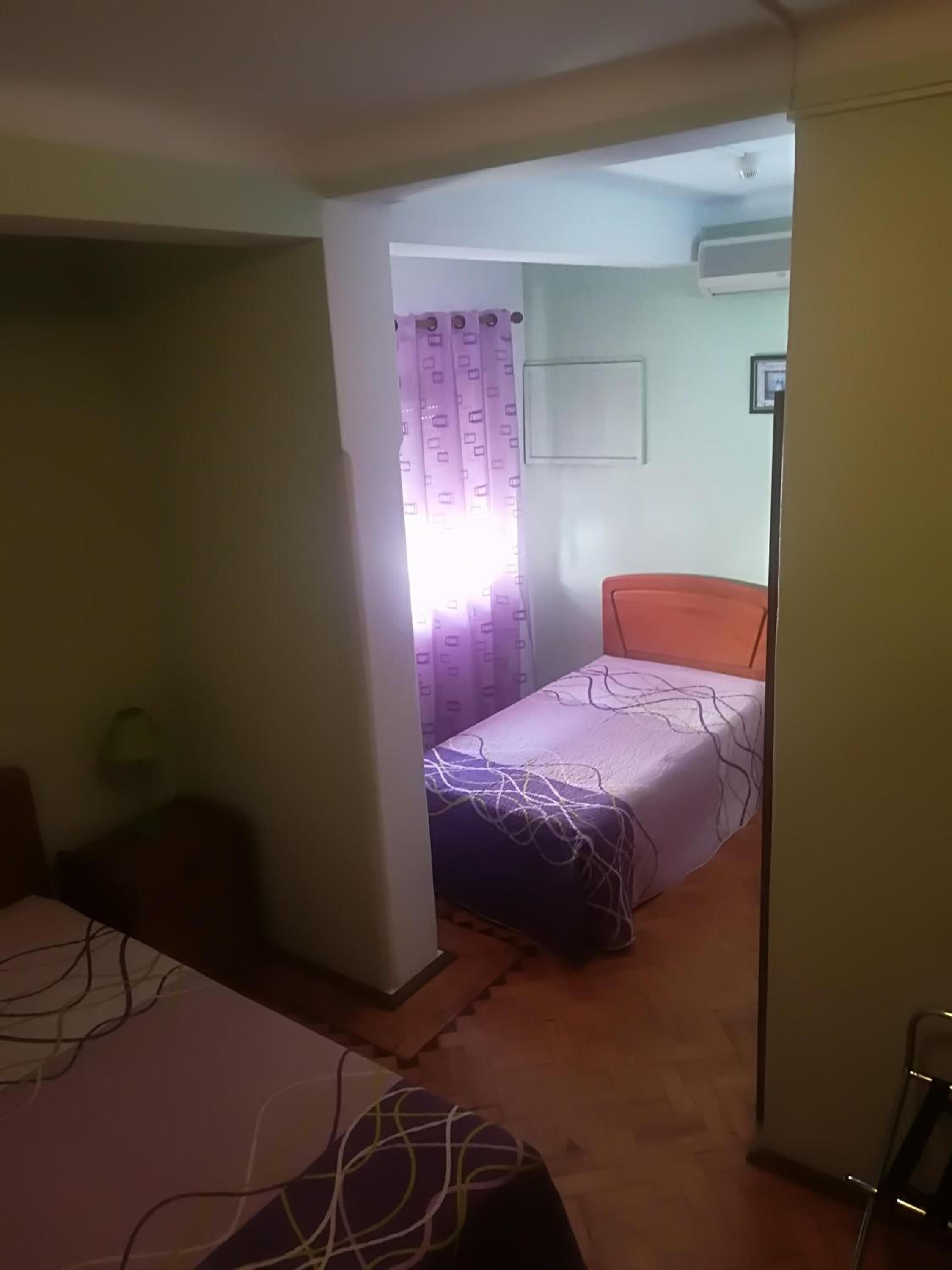 Una habitación pequeña y tenuemente iluminada, con una cama individual, una silla y un escritorio.