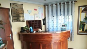 Uma receção com bancada de madeira, um mural de avisos e uma janela com cortinas.