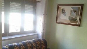 A living room with a patterned sofa, a framed picture on the wall, and a window with blinds. - Hotel Conforto Latino (Abrantes)