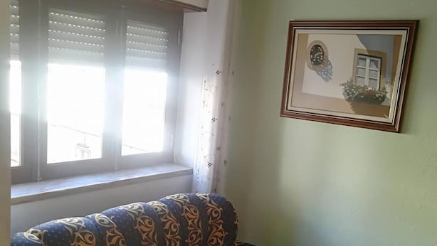 Uma sala de estar com um sofá estampado, um quadro na parede e uma janela com persianas.