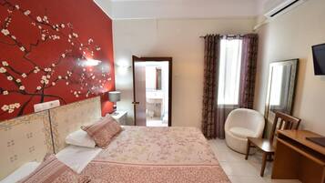 A hotel room with a bed, a chair, a desk, a TV, and a bathroom visible through an open door.