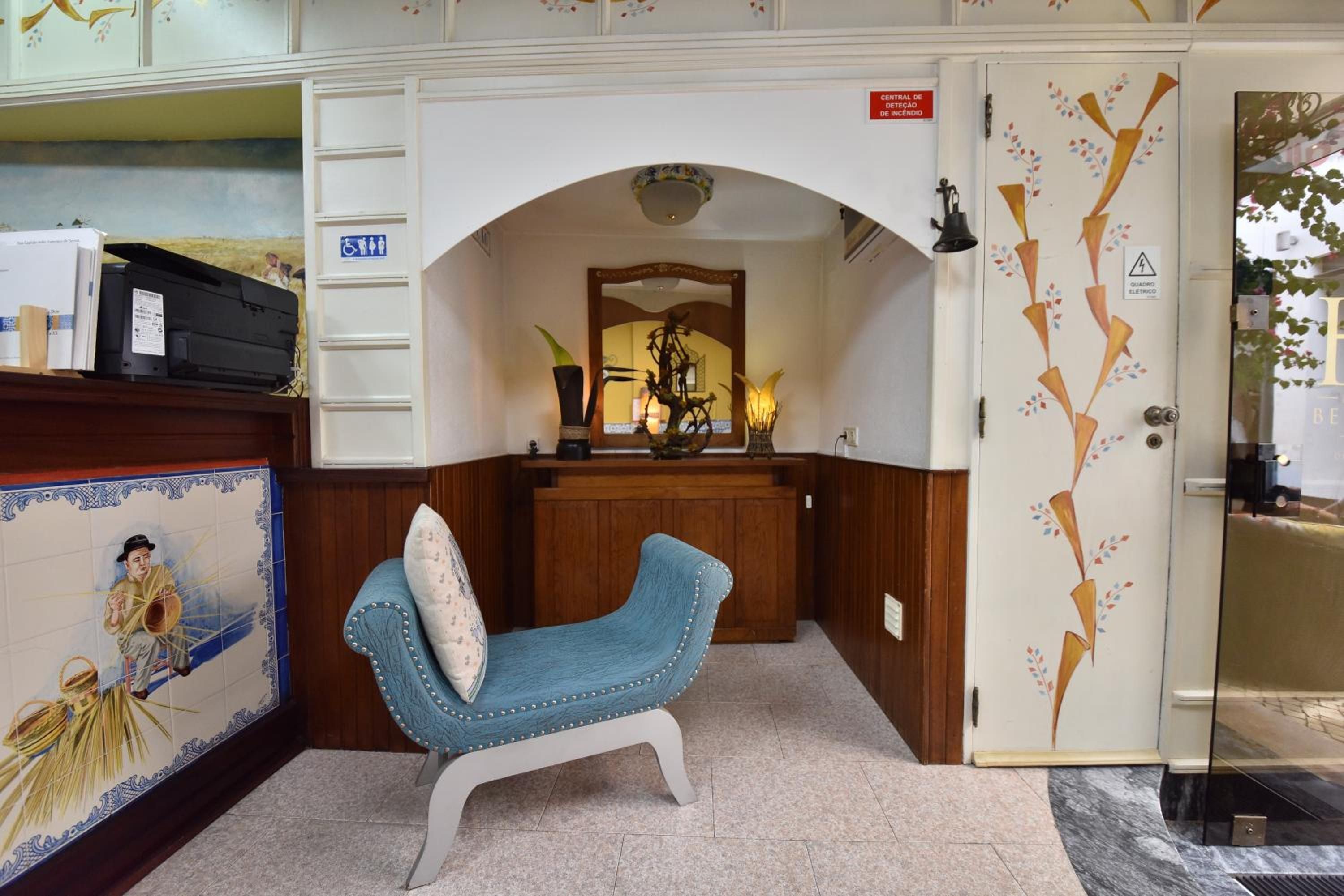 A room with a blue armchair, a wooden desk with a computer, a mirror, and a decorative door.