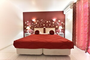 Cama doble con colcha roja, dos lámparas de noche y un diseño floral en la pared.